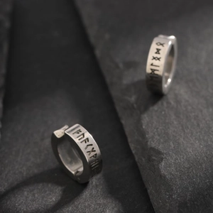 Macro detail of silver titanium steel ear clips with engraved black Norse runes on dark rock