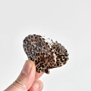 Minimalist shell-shaped hair claw clip with leopard pattern finish held by hand