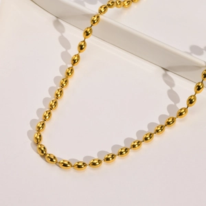 Detail of a golden titanium steel beaded necklace with oval pearls on white background