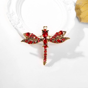Vintage gold dragonfly brooch with deep red crystals on an elegant white relief plate