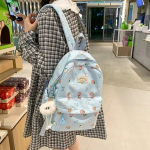 Cute light blue strawberry pattern backpack with plush ball charm shown on a model