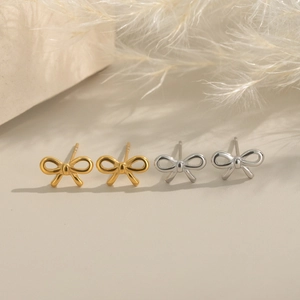 Elegant bow-shaped gold and silver stainless steel earrings on a minimalist stone background