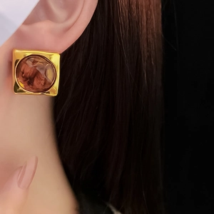 Close-up of irregular brown geometric resin earrings with a gold-tone metallic frame