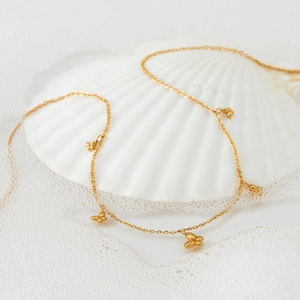 Elegante goldene Schmetterlingskette auf weißer Muschel mit Wasser- und Schaumdetail