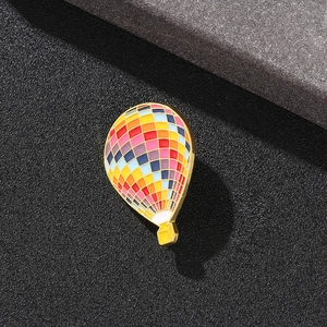Macro detail of a golden hot air balloon brooch with colorful enamel patterns on grey background