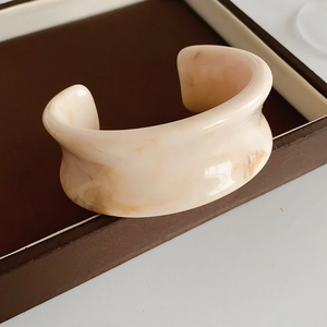 Close-up of wide resin open bangle with beige marble texture on a dark display tray