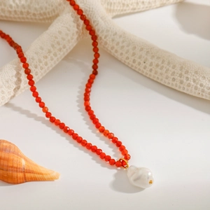 Close-up of beaded necklace with orange beads and a baroque pearl on a sea-themed background