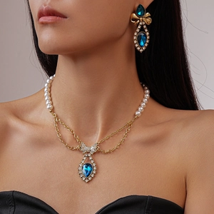 Vintage gold necklace set with blue teardrop gems, pearls, and crystal bow accents