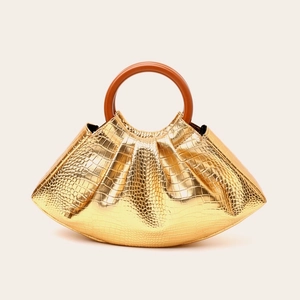 Detail of evening bag featuring gold crocodile texture and round wooden handle