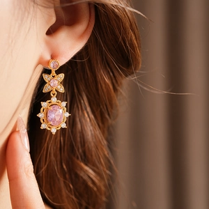 Detail of vintage style gold earrings featuring oval pink zircon and sparkling bow accents