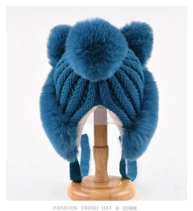 Detail of teal knit winter hat with thick cable pattern and three soft faux fur pom-poms