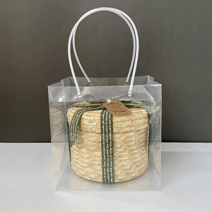 Detail of round straw gift box with green ribbon and clear PVC carrying bag
