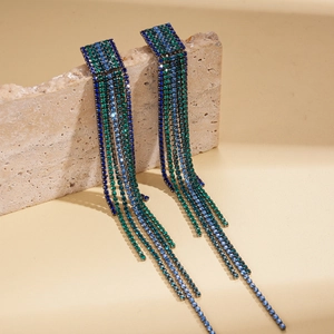 Long blue and green rhinestone tassel earrings on a textured stone display