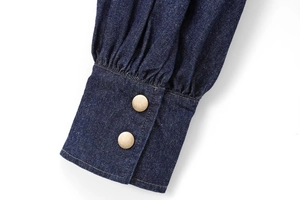 Close-up of deep blue denim shirt cuff with vintage bronze metal buttons and fine stitching