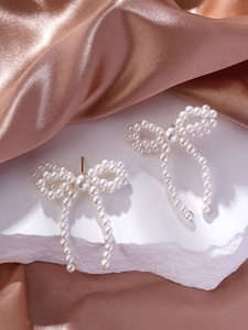 Detail of bow-shaped pearl earrings with elegant long tassels on a stone display