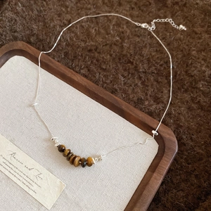 Detailed close-up of tiger eye stone beads on a silver chain over a wooden tray