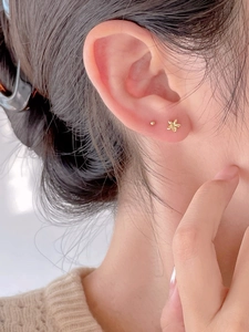 Detailed shot of golden flower and stud earrings on ear with elegant metallic texture
