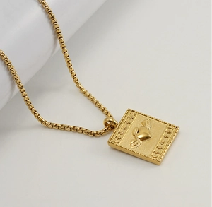 Détail du pendentif rectangulaire en acier doré 18K avec cœur d'ange et étoiles gravés