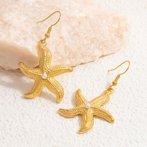 Macro shot of 18k gold starfish earrings with central pearl on textured background