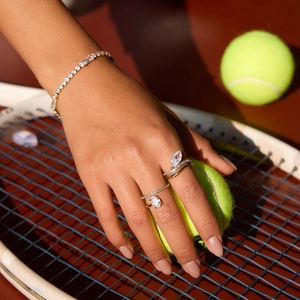 Dettaglio del bracciale tennis scintillante e anelli d'oro sulla mano su sfondo campo da tennis