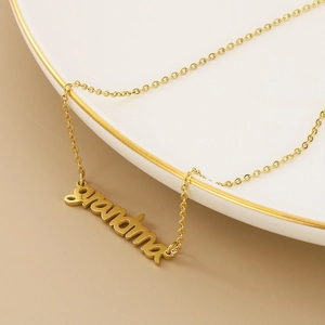 Close-up of golden cursive grandma pendant necklace on a decorative ceramic plate