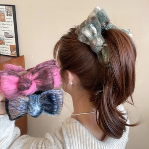 Detail view of large tweed bow hair clips in green, purple, and blue worn on a ponytail