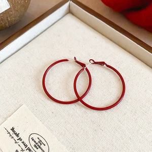 Detail of large red metal hoop earrings on a beige tray with artistic card and warm lighting