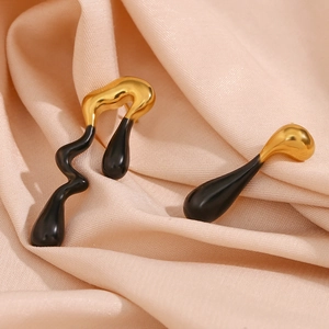 Detail of asymmetrical lava gold and black enamel earrings on beige satin background
