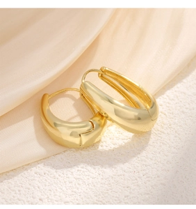 Macro view of gold-plated U-shaped earrings with polished finish on silk fabric