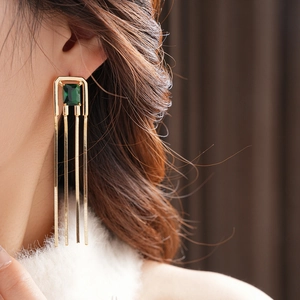 Close-up of gold fringe earrings with square emerald green stones on a model