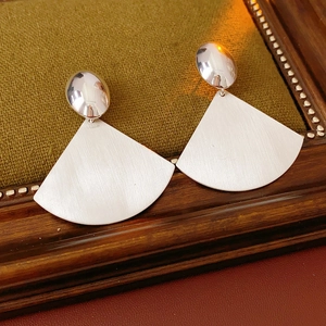 Detailed view of silver oval brushed metal earrings on a vintage wooden frame backdrop