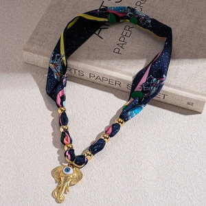 Close-up of silk scarf necklace with golden elephant pendant and evil eye charm