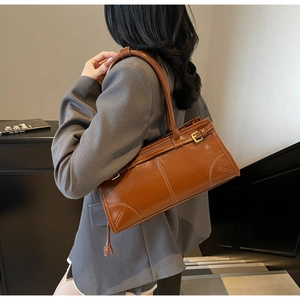 Detail of a brown leather shoulder bag featuring white contrast stitching and gold hardware