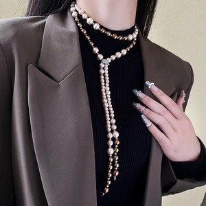 Detail of a long Y-shaped necklace with gold and cream pearls on a classic blazer outfit