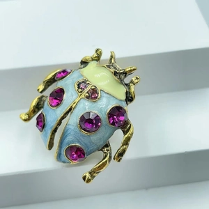Macro shot of beetle brooch with light blue enamel wings and rose red rhinestones on white