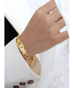 Detail view of a gold-tone watchband link bracelet on a model wearing white sleeves