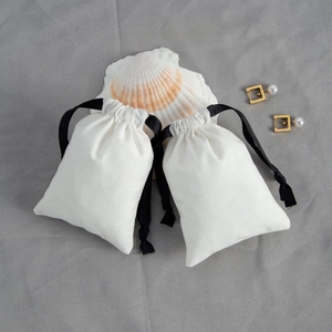 White cotton jewelry drawstring pouch with black ribbon shown with seashells and pearls
