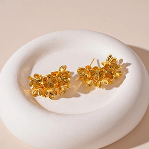 Macro shot of gold floral cluster earrings on a white stone pedestal with soft lighting