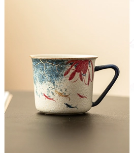 Detail of ceramic coffee mug featuring hand-painted koi fish and floral patterns with gold trim