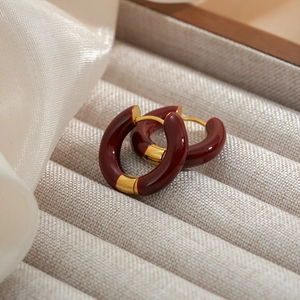 Close-up of burgundy enamel C-shaped hoop earrings with gold-plated metal accents