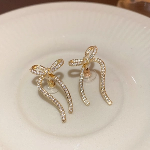 Elegant gold bow earrings with sparkling cubic zirconia on a minimalist ceramic tray