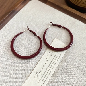 Close-up of dark red geometric hoop earrings on a minimalist wooden tray display