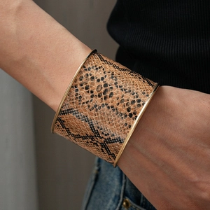 Close-up of a wide leopard print open cuff bracelet with metallic gold trim on a model