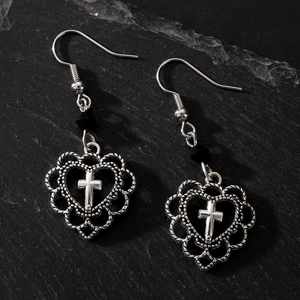 Macro view of gothic silver cross earrings with heart lace edges on stone background