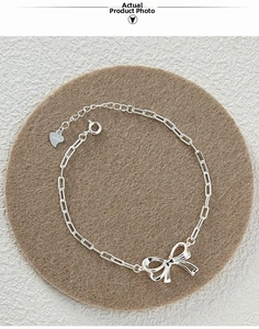 Detailed macro of S925 sterling silver bow charm bracelet with paperclip chain and heart tag