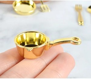Close-up of a tiny golden miniature frying pan held in hand for scale and detail