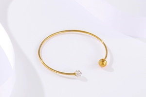Détail d'un bracelet ouvert doré avec une sphère sertie de cristaux et une bille dorée lisse