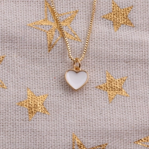 Close-up of golden box chain with white enamel heart pendant on starry fabric