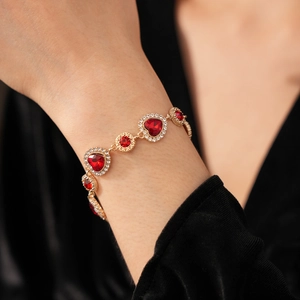 Dettaglio del bracciale vintage in oro con gemme rosse a cuore e diamanti sul polso