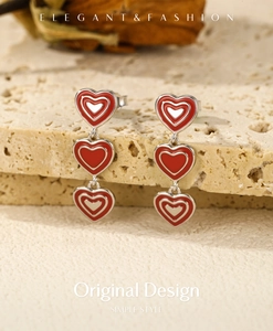Macro detail of red enamel heart drop earrings on a natural stone surface